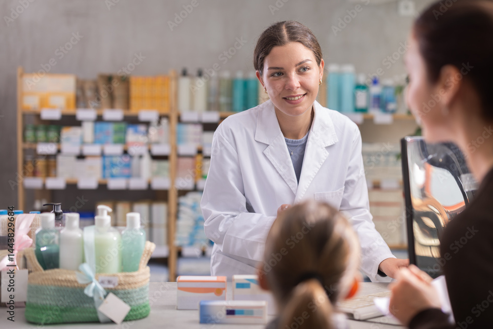Obraz premium Polite young female pharmacist offering medicament to mother with daughter in chemist's shop