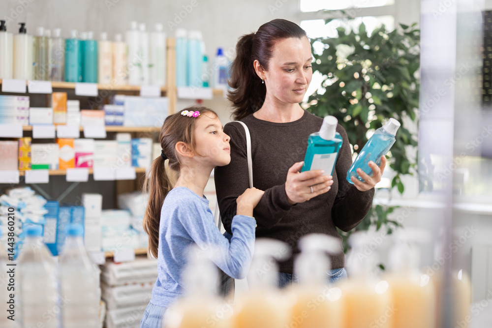 Adult woman with daughter buyers choosing bottle of mouthwash in pharmacy