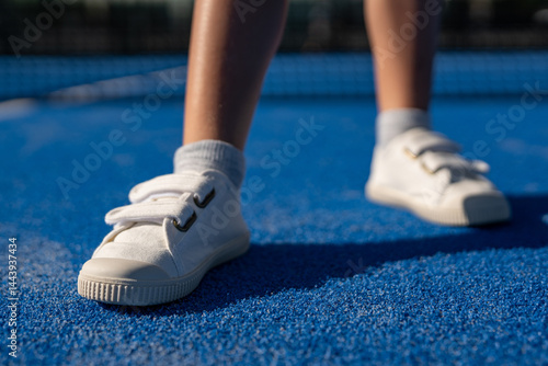 Bild auf Leinwand Close-up of white velcro sneakers on blue padel court surface with soft sunlight