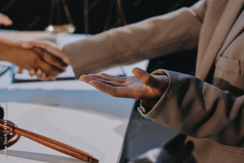 Fototapeta premium Two businesspeople are shaking hands in a law office with a scale and a gavel on the table.