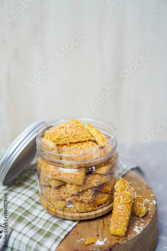 an open jar filled with cheese cookies and some cookies outside with gingham fabric and wooden pedestal below it
