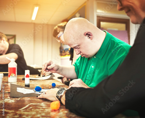 Quadro su tela Therapist helping man with down syndrome in disability support group or daycare for disabled people