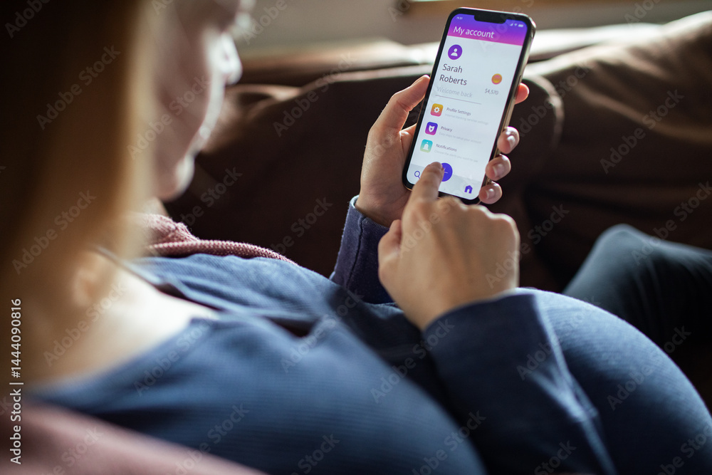 Pregnant woman using mobile banking app on smartphone while relaxing on couch