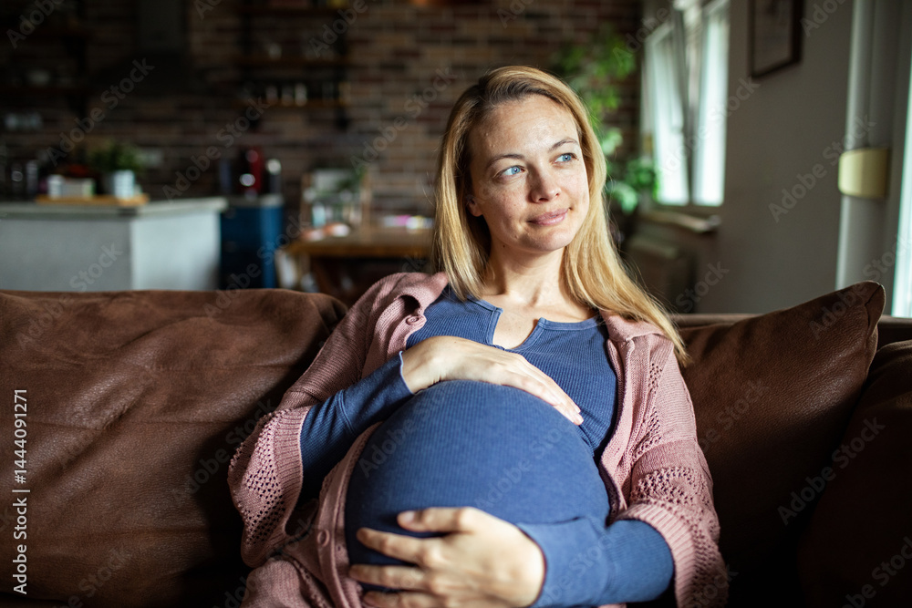 Pregnant woman sitting on couch smiling and holding her belly