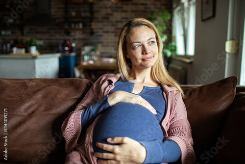 Obraz na płótnie Pregnant woman sitting on couch smiling and holding her belly w salonie