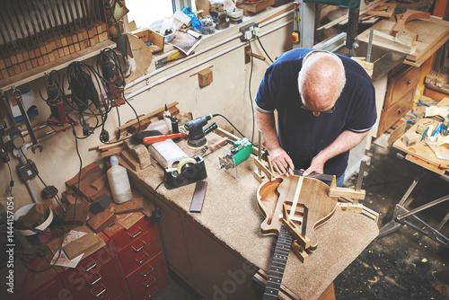Creative and skilled carpenter making a guitar out of wood in a workshop. Above view of senior professional entrepreneur craftsman or expert artisan making an instrument in woodwork carpentry shop