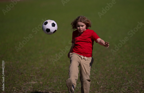 Obraz na płótnie A kid is playing football. A child kicks the soccer ball. Kids sport. Kid football player runs toward goal. Kid kicking football ball. A sporty child enjoys the football. Kids are playing foot ball. w salonie