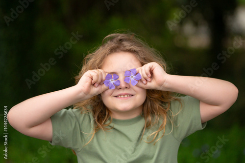 Obraz na płótnie Spring flowers near child face. Kid in blooming spring garden. Child face close-up, covering eyes with spring flowers. Dreamy kid face in spring orchard. Playful kid covering his eyes with flowers. w salonie