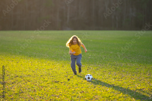 Obraz na płótnie Child playing soccer. Kid boy kicking a football on the grass. Kid running with a soccer ball. Playful children enjoying a football game. Kids soccer match. Kid playing soccer kicking a ball. w salonie