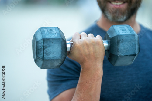 Dumbbells in arm. Closeup of a mature man lifting dumbbells outdoors. Man arm muscles engaged in a dumbbell workout. Arms hold dumbbell. Closeup of a male arm with dumbbell.