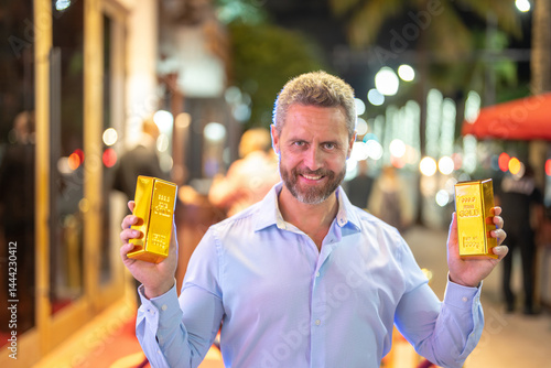 Obraz na płótnie Business man holding a gold bar and cash. Gold financial success. Successful rich man holding gold and money. Business man with gold bars. Golden treasure. Hands hold golden bars and cash. w salonie