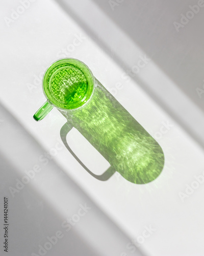 Obraz na płótnie Green colored glass cup with artistic light reflections and caustics on white table. Clear mug for tea and coffee at sunlight with window shadow, summer drink concept, minimal style photo, copyspace w salonie