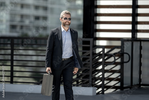 Obraz na płótnie Successful businessman walking outdoors with a briefcase. Businessman on the go. Mature lawyer in a suit. Rich businessman with briefcase. Middle-aged businessman on way to work. Handsome lawyer. w salonie