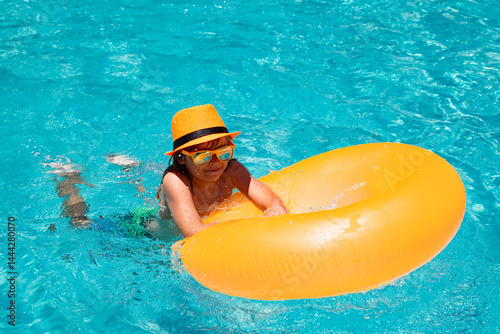 Kid swim with floating ring in swimming pool. Kids summer vacation. Happy child boy with inflatable ring in poolside.