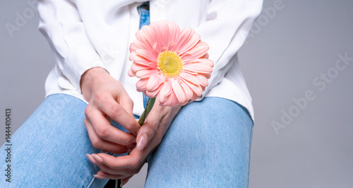Young woman with pink flower on bright studio background, ideal for beauty, style and naturalness concepts