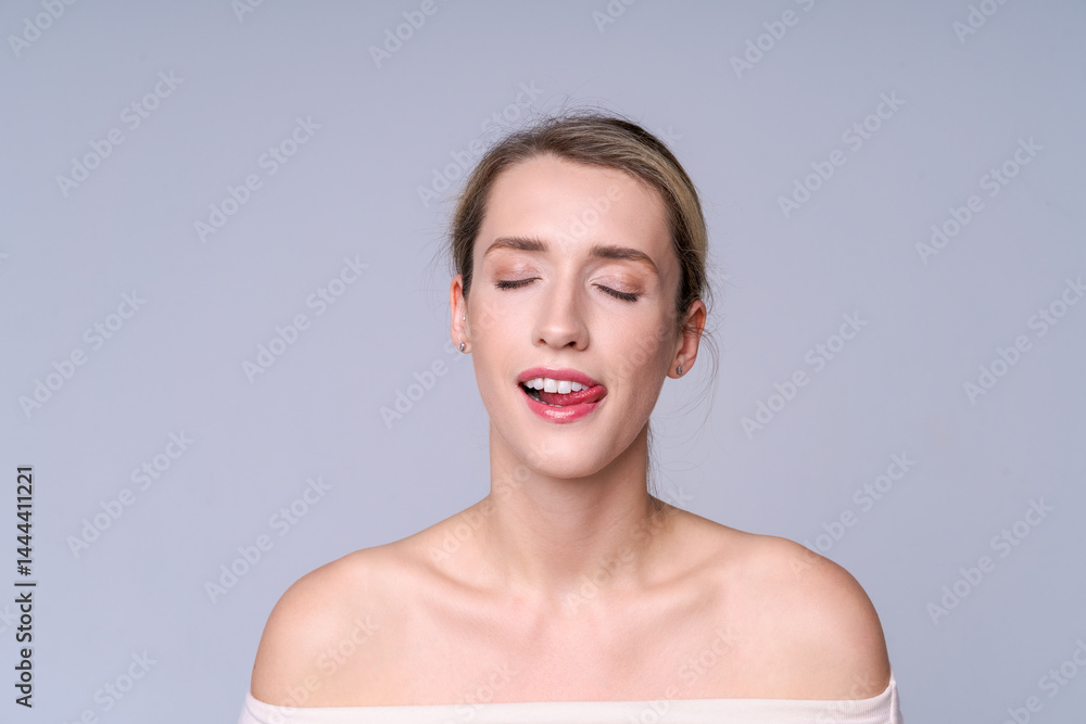 Cheerful young woman winking and sticking out tongue expressing playful mood and joy on neutral light background. Concept of happiness, youth and lightness