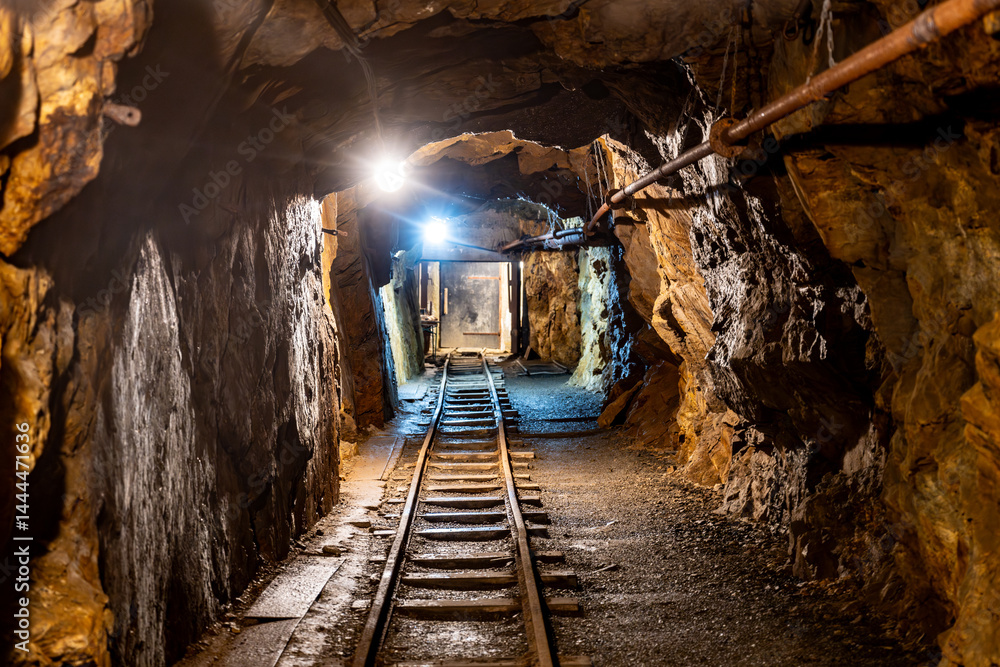 Naklejka premium This mine shaft in Jachymov, Czechia showcases the rich mining history of the area. Dimly lit tunnels lead into the depths, revealing tracks used for transporting minerals.