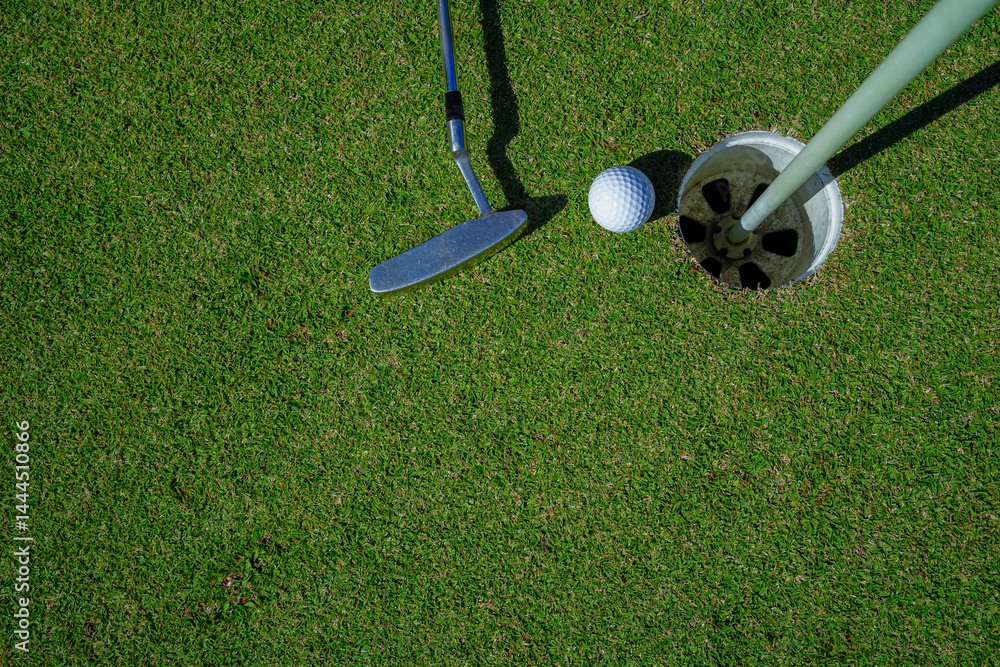 Obraz premium Top view of a golf ball with putter on green course at hole.
