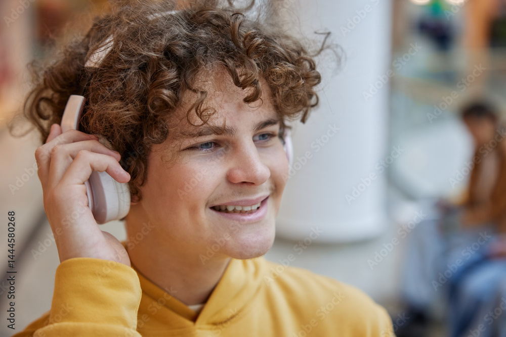 Teenage boy listening to music in headphones over shopping mall background