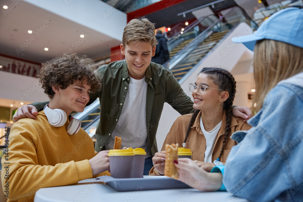 Teenage friends resting having refreshments at cafeteria in shopping mall
