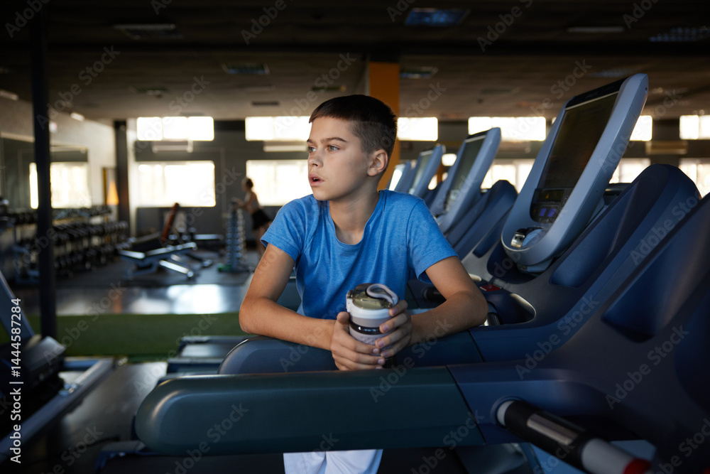 Pensive tired boy relaxing after cardio training on treadmill at sport club