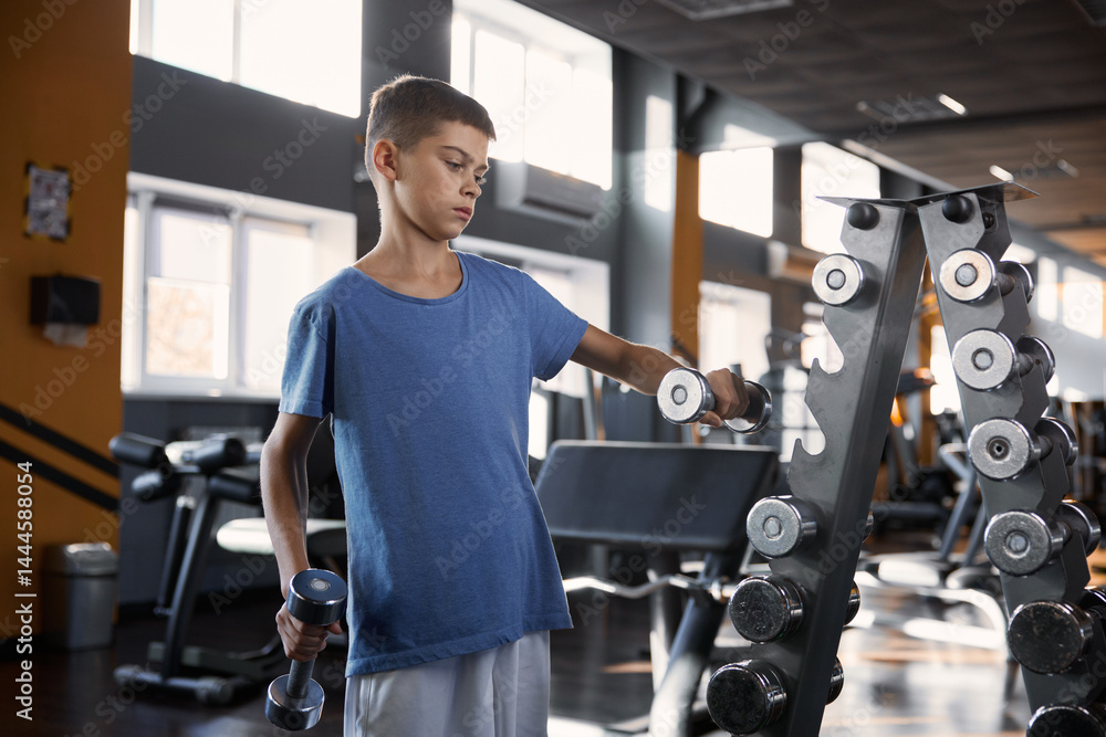 Teenage boy choosing dumbbell weight for training workout at gym