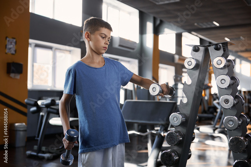 Obraz na płótnie Teenage boy choosing dumbbell weight for training workout at gym w salonie