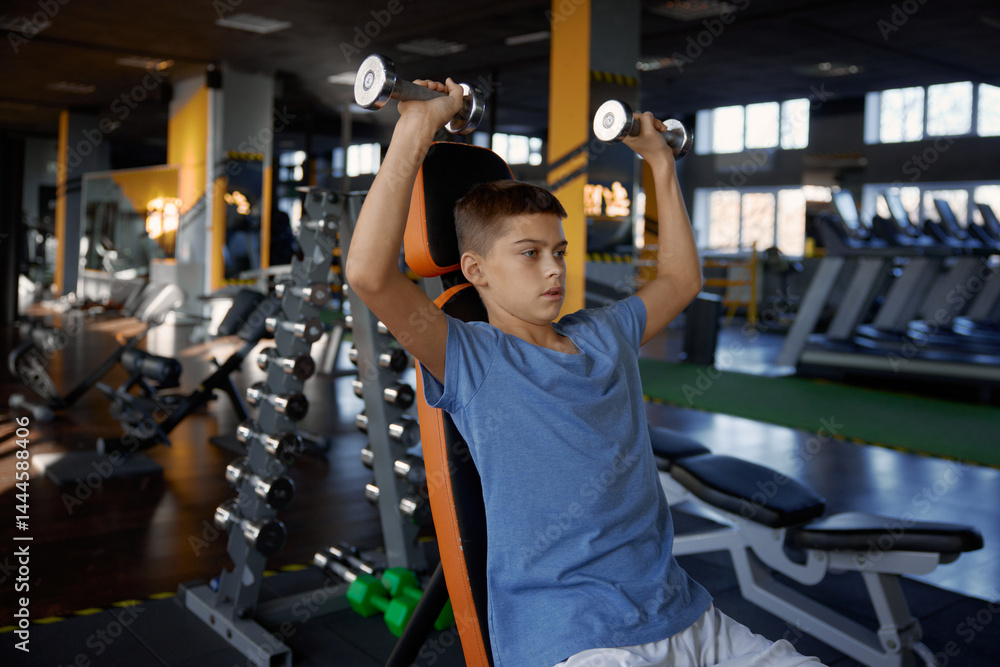 Teenage boy lifting dumbbells enjoying sportive workout at gym
