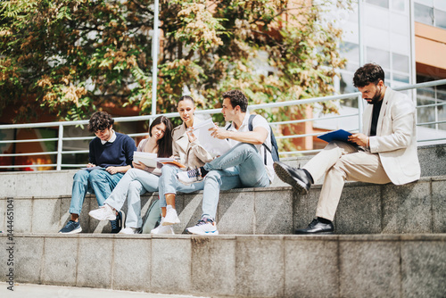 A group of high school students work together on assignments while seated outdoors. A professor provides guidance, creating a collaborative and educational atmosphere. The natural setting adds to the