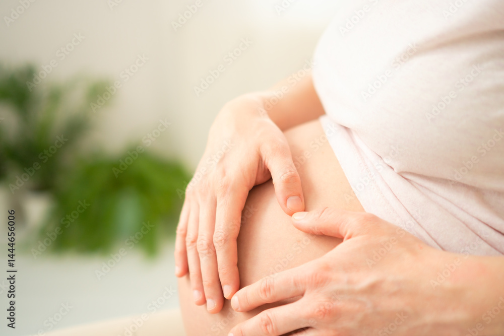 Naklejka premium Close-up of a pregnant woman gently holding her belly, forming a heart shape with her hands. The image conveys a sense of love, anticipation, and maternal connection. Pregnancy time