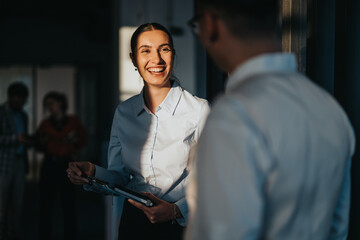 A diverse group of business people engaging in a friendly conversation in an office hallway. The image captures a positive and collaborative work environment with multicultural colleagues.