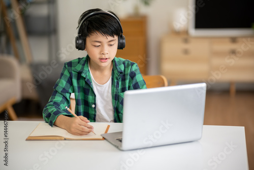 A boy is studying online intently on his laptop at home.
