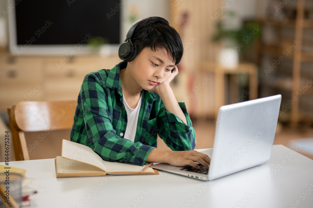 A boy is studying online intently on his laptop at home. A boy is studying online intently on his laptop at home.