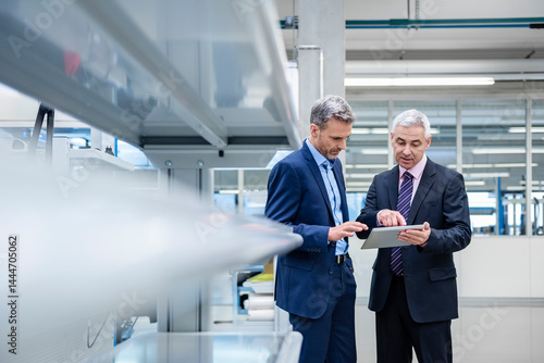 Business executives discussing strategy in a production hall using a tablet