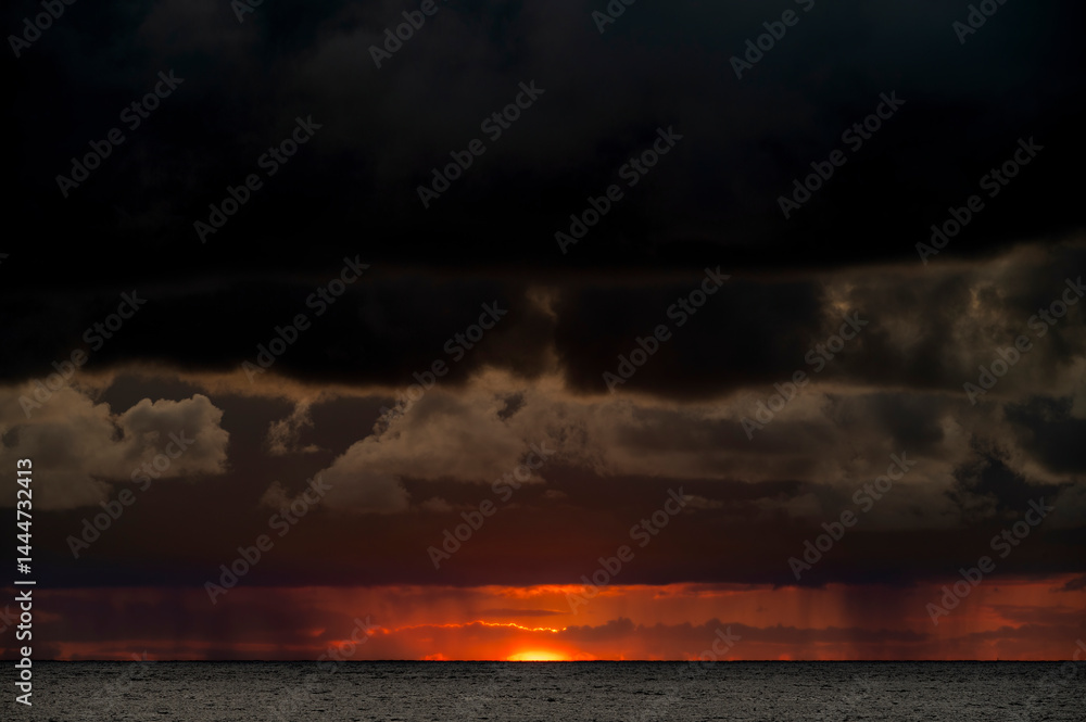 Very moody and dramatic sky over the cloudy ocean horizon, with strong orange, sunbeams and traces of lingering storm cells