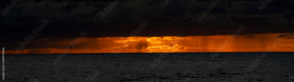 Very moody and dramatic sky over the cloudy ocean horizon, with strong orange, sunbeams and traces of lingering storm cells