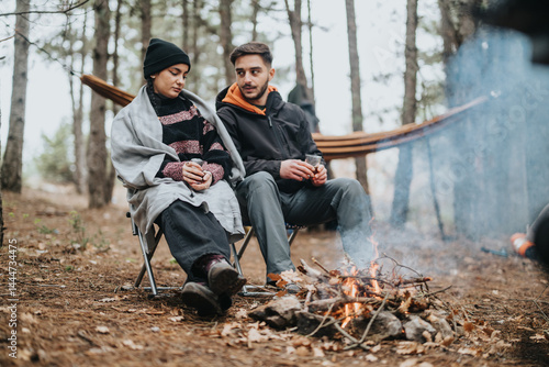 A cozy scene of two friends having a picnic by a campfire during winter in the mountains, surrounded by a serene forest.
