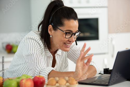 smiling woman in headset waving hand at laptop