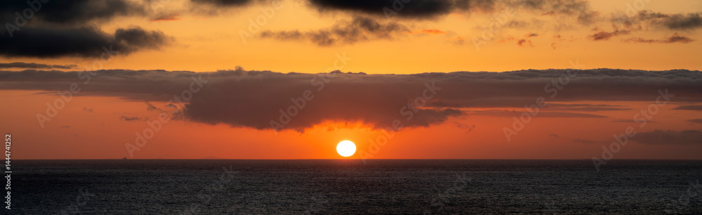 Very moody and dramatic sky over the cloudy ocean horizon, with strong orange, sunbeams and traces of lingering storm cells