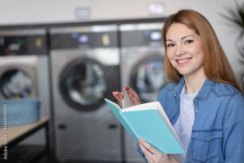 happy female reading book while doing her washing in laundromat