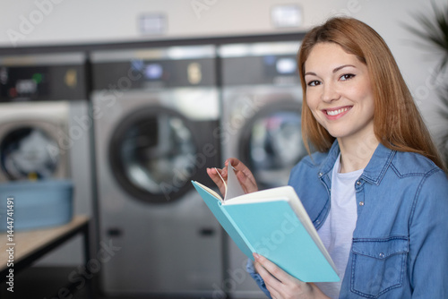 Obraz na płótnie happy female reading book while doing her washing in laundromat w salonie