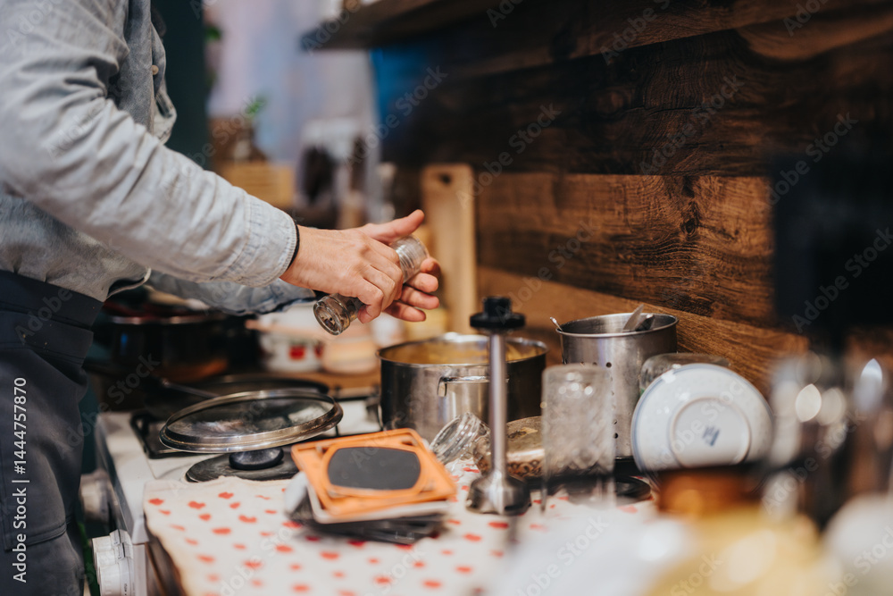 A person cooking in a well-used kitchen with rustic decor, focusing on meal preparation and seasoning. The image evokes a sense of warmth, creativity, and the joy of cooking at home.