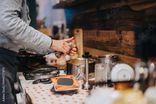 Obraz na płótnie A person cooking in a well-used kitchen with rustic decor, focusing on meal preparation and seasoning. The image evokes a sense of warmth, creativity, and the joy of cooking at home. w salonie