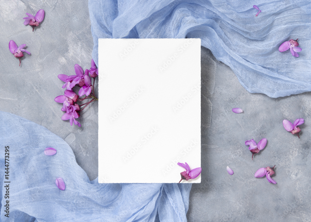 Vertical blank card on fabric near wild purple flowers top view on gray, spring wedding mockup