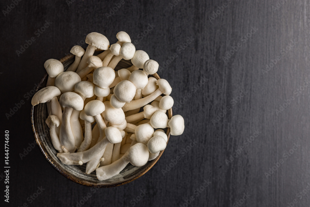 Raw white shimeji mushrooms on black table. Top view.