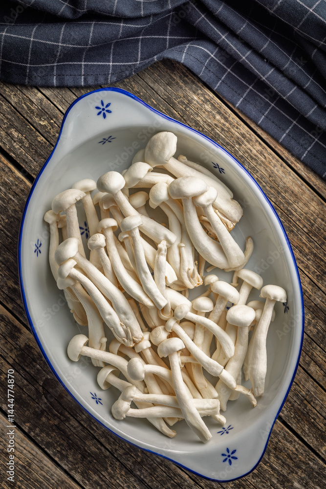 Raw white shimeji mushrooms in bowl on wooden table. Top view.
