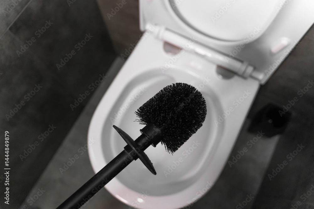 Modern black toilet brush hovering over an open white toilet bowl, preparing for cleaning in a contemporary bathroom featuring a stylish gray tiled floor