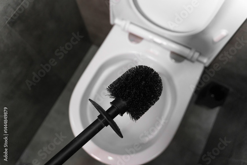 Modern black toilet brush hovering over an open white toilet bowl, preparing for cleaning in a contemporary bathroom featuring a stylish gray tiled floor