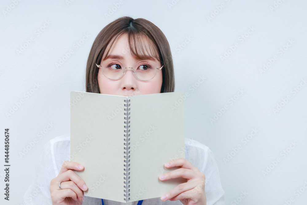 ノートで顔を隠す眼鏡をした若い女性 ノートで顔を隠す眼鏡をした若い女性