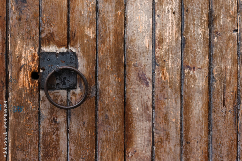 Close-up of an aged wooden door featuring a metal ring handle